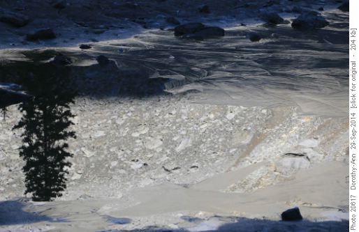 Reflection of mountain slope beside skim ice of lake